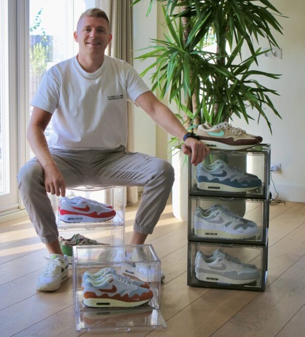 Een man zit op een sneakerbox met Air Max 1 sneakers naast een plant.