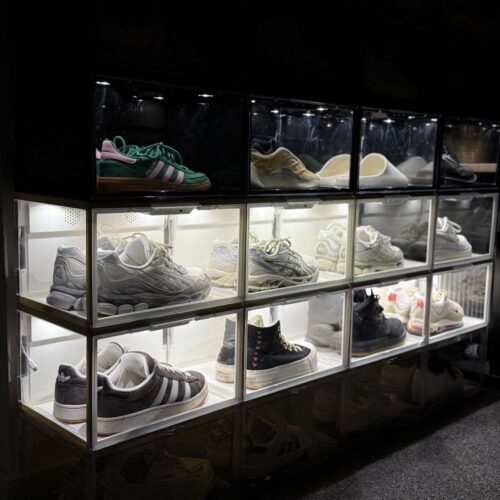 Twaalf sneakerdisplayboxen in LED wit en zwart in een 4x3-opstelling, deels met LED-verlichting, gevuld met diverse Adidas-, Asics-, Converse- en Nike-modellen, oplichtend in een donkere ruimte.