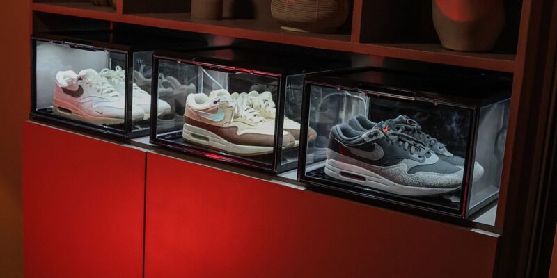 Drie verlichte zwarte sneakerdisplayboxen met LED-verlichting, gevuld met Nike Air Max 1's, op een houten kast met decoratieve vazen erboven en rode sfeerverlichting.
