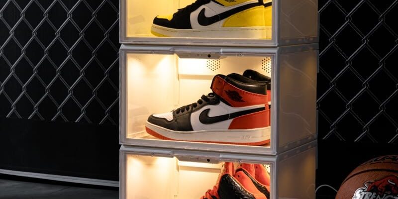 Drie verlichte transparante sneakerdisplayboxen met witte rand en warme LED-verlichting, op elkaar gestapeld met high-top Air Jordan 1's, naast een basketbal tegen een donkere achtergrond.
